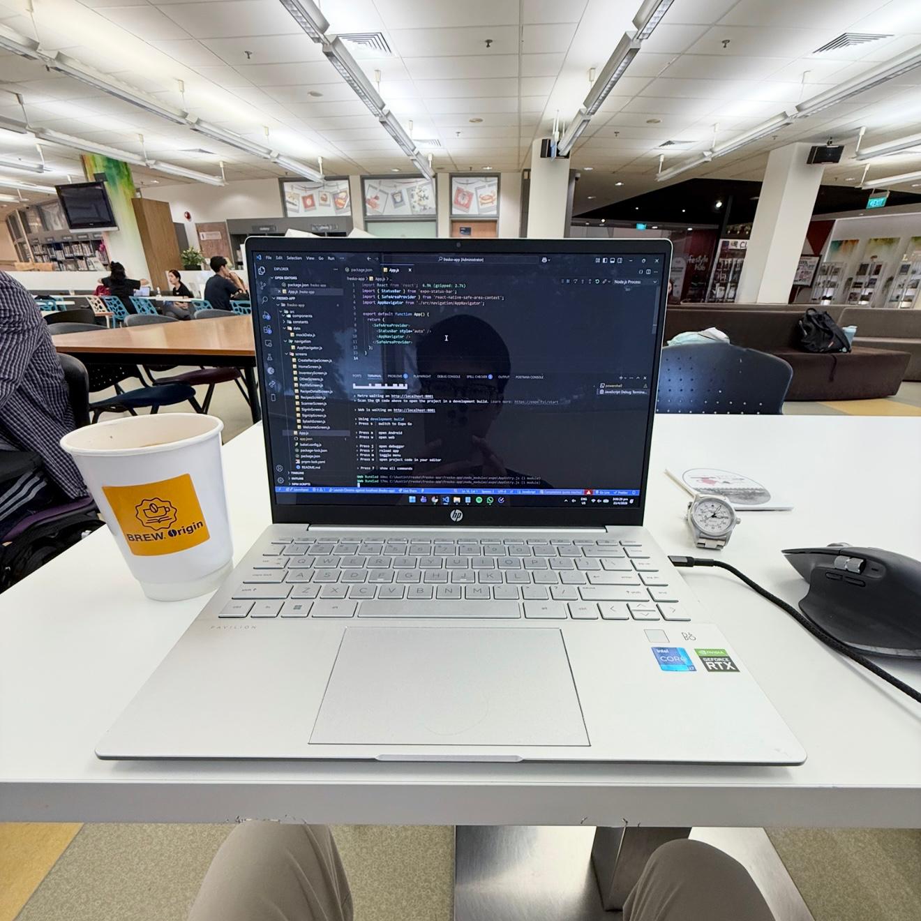 My laptop showing code in an editor, on a library table beside a cup of coffee